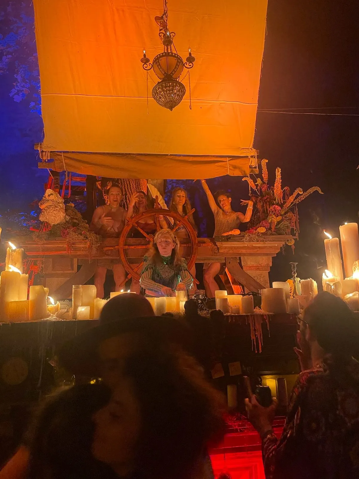 Daniela DJing at a ship's wheel under an orange sail, surrounded by candles, on the Fairy Forest stage at CAMP Festival 2025