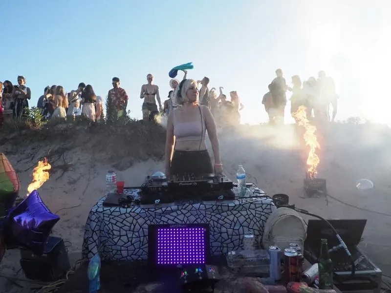 Daniela playing a sunrise set on Plumb Beach in Brooklyn with dancers on the dunes behind her, 2024