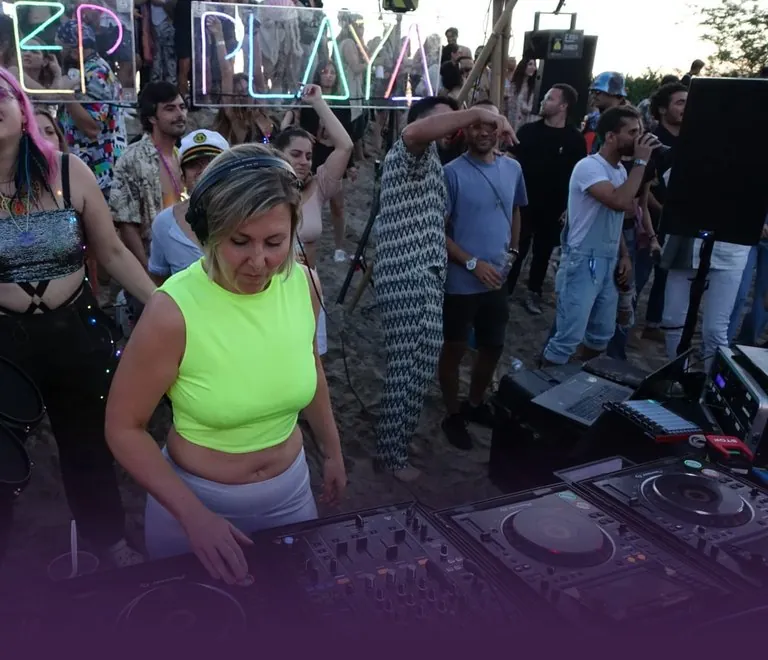 Daniela at the decks at a Deep Playa beach party, neon sign behind